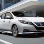A 2021 White Nissan Leaf driving by an office building_mobile