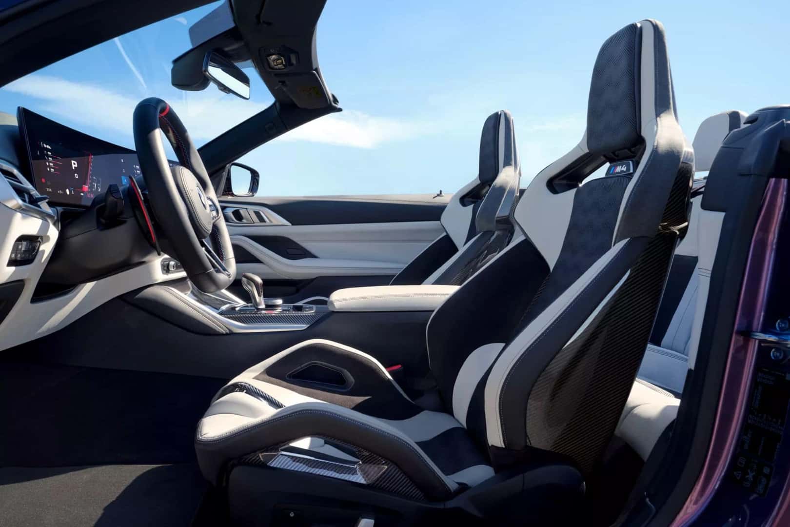 BMW M4 convertible interior featuring white and black sport seats with a scenic open sky in the background.