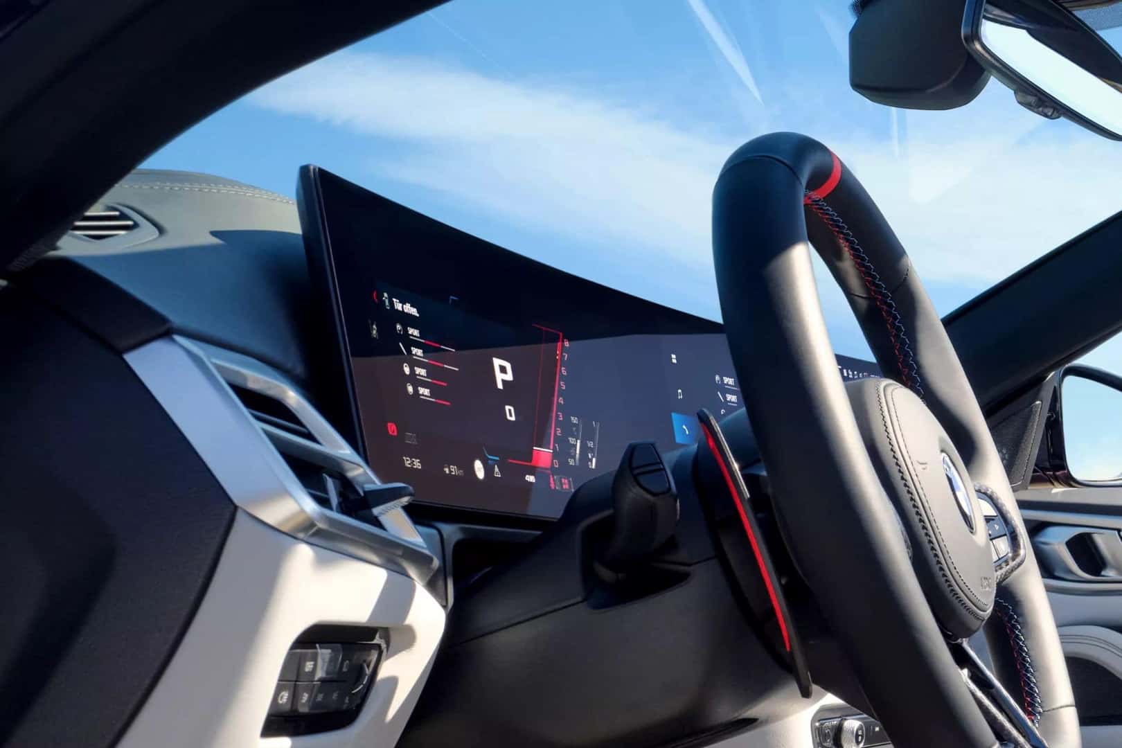 Close-up of the BMW M4 convertible's digital cockpit and steering wheel under a clear blue sky.
