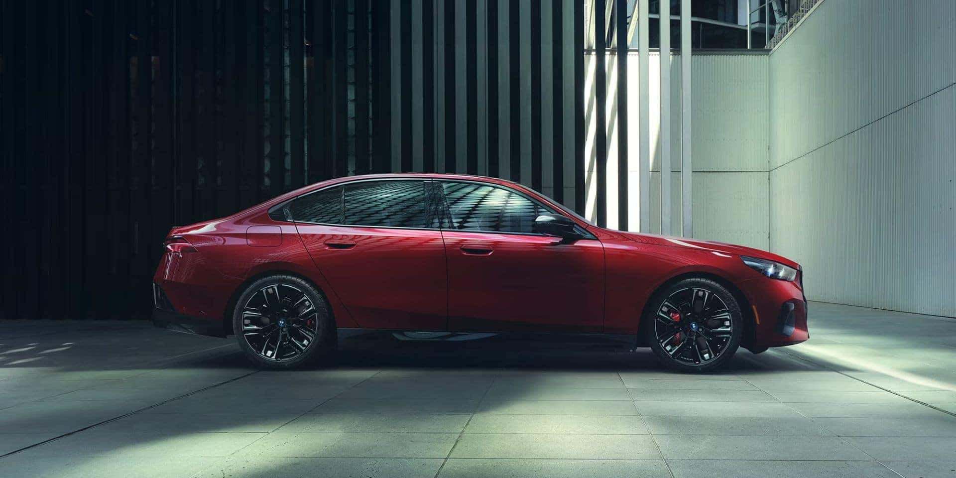 Side profile of a red BMW i5 M60 electric sedan in a modern showroom.