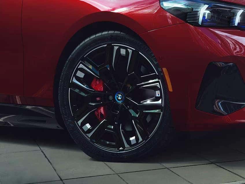 Close-up of BMW i5 M60 black alloy wheels with red brake calipers.
