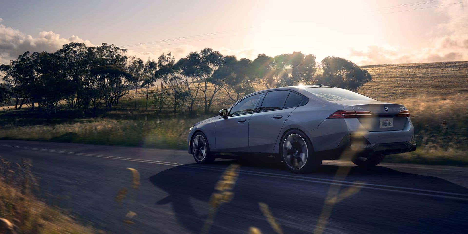 BMW i5 eDrive40 sedan driving on an open road with scenic countryside in the background.