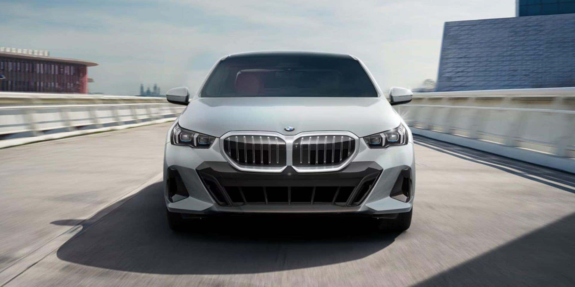 BMW 5 Series sedan in white, driving on a bridge with modern architecture in the background.