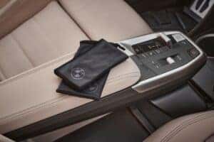 Close-up of a BMW vehicle's center console with beige leather armrest and black BMW-branded microfiber pouches.