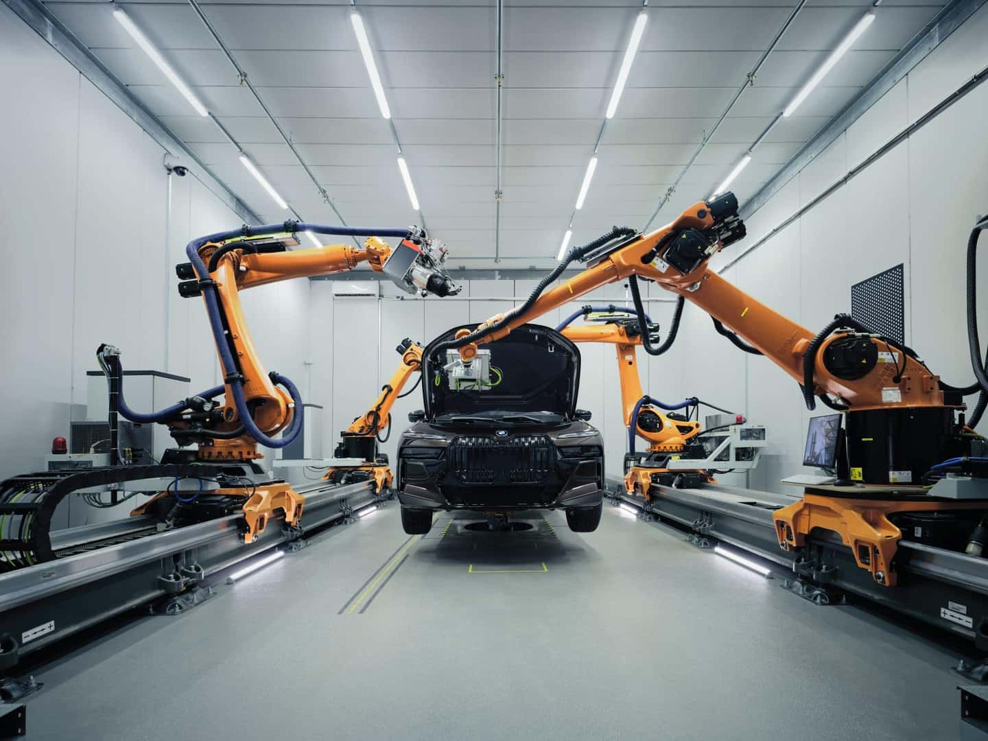 Automated robotic arms assembling a black BMW in a high-tech manufacturing facility.