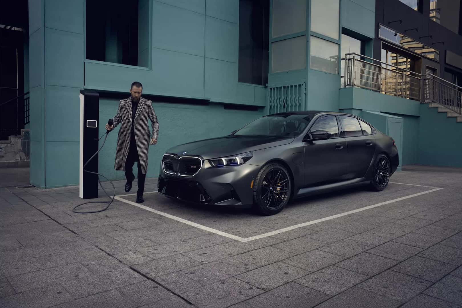 Man in long coat preparing to charge a dark gray BMW 5 Series Plug-in Hybrid at a street charging station