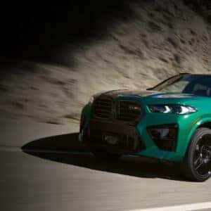Front view of a green 2026 BMW X5 M driving on a mountain road