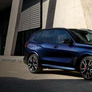2026 BMW X5 M60i in blue parked in front of a modern building with angular architecture
