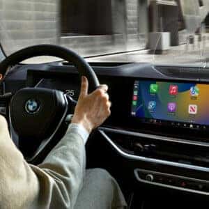 Woman driving a 2026 BMW with Apple CarPlay apps displayed on the infotainment screen