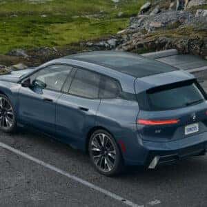 a blue 2026 bmw ix parked in a parking space overlooking a green mouintainous terrain.
