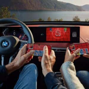 two people in the front seats playing uno on their phones with the curved display screen showcasing uno as well on a 2026 iX