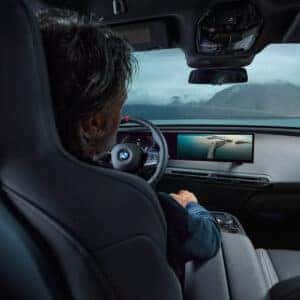 a man driving a bmw iX looking at the curved display screen.