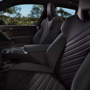 the interior driver's side view of a 2026 bmw iX M70 featuring black leather interior with a blue and red line going across the the front seats.