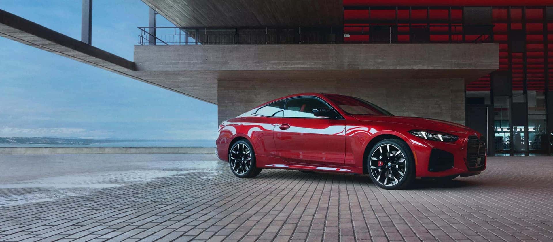 a red bmw 4 series coupe parked undernearth a bridge