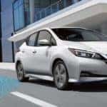 A 2021 White Nissan Leaf driving by an office building