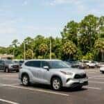 Silver Toyota Highlander parked in a nearly empty asphalt parking lot with green trees in the background.