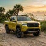 Yellow Nissan Frontier PRO-4X parked on a sandy beach at sunset with palm trees in the background.