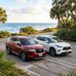 A red Nissan Pathfinder Rock Creek and a white Toyota Highlander parked on a coastal road.