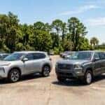 A silver Nissan Rogue SUV and a grey Nissan Frontier pickup truck parked on a sunny dealership lot.
