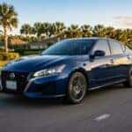 Blue Nissan Altima driving on a palm tree-lined road during sunset.