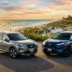 A silver Nissan Rogue and a dark blue Toyota RAV4 parked on a coastal road at sunset.