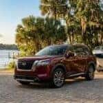 Red Nissan Pathfinder towing a boat on a paved driveway near a lake with palm trees.