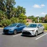 Blue Nissan Versa and silver Toyota Corolla parked side-by-side in a sunny asphalt lot.