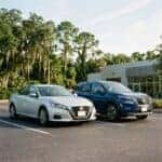 A silver Nissan sedan and a blue Nissan SUV parked side-by-side in a sunny asphalt parking lot. (Representative image for illustration purposes only. Actual vehicle may vary based on trim and configuration.)