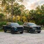 A blue Nissan Frontier and a grey Ford Ranger parked side-by-side on a gravel path in a wooded clearing. (Representative image for illustration purposes only. Actual vehicle may vary based on trim and configuration.)