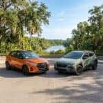 An orange Nissan Kicks and a green Subaru Crosstrek parked side-by-side at a scenic overlook overlooking a river. (Representative image for illustration purposes only. Actual vehicle may vary based on trim and configuration.)