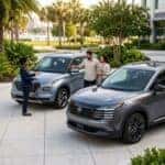 A car salesperson showing a light blue SUV to a couple in an outdoor dealership lot surrounded by palm trees. (Representative image for illustration purposes only. Actual vehicle may vary based on trim and configuration.)