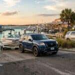 A blue SUV backing a boat on a trailer down a concrete boat ramp at a sunny coastal marina. (Representative image for illustration purposes only. Actual vehicle may vary based on trim and configuration.)