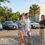 A young couple talks with a dealership representative in a car lot with Nissan vehicles. (Representative image for illustration purposes only. Actual vehicle may vary based on trim and configuration.)