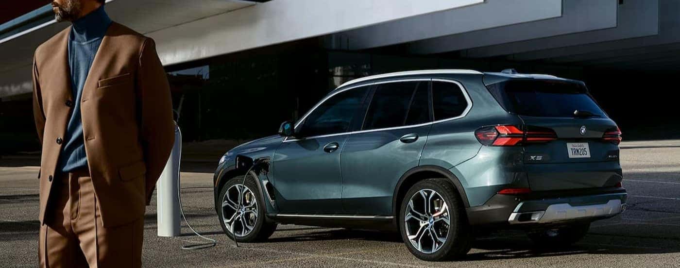 A green 2025 BMW X5 is shown charging near a person.