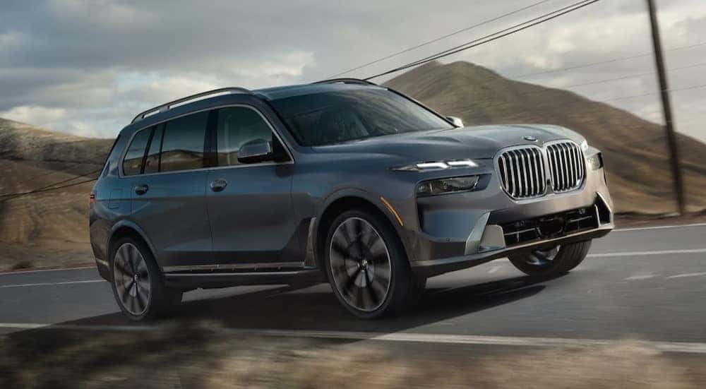 A gray 2025 BMW X7 is shown driving on a highway.