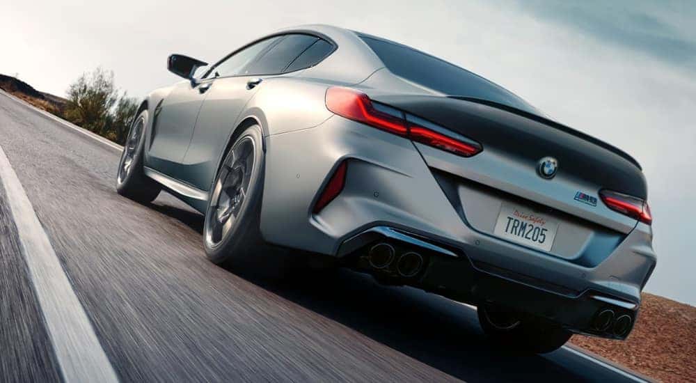 A silver 2025 BMW M8 Gran Coupe is shown from the rear driving on an open road.