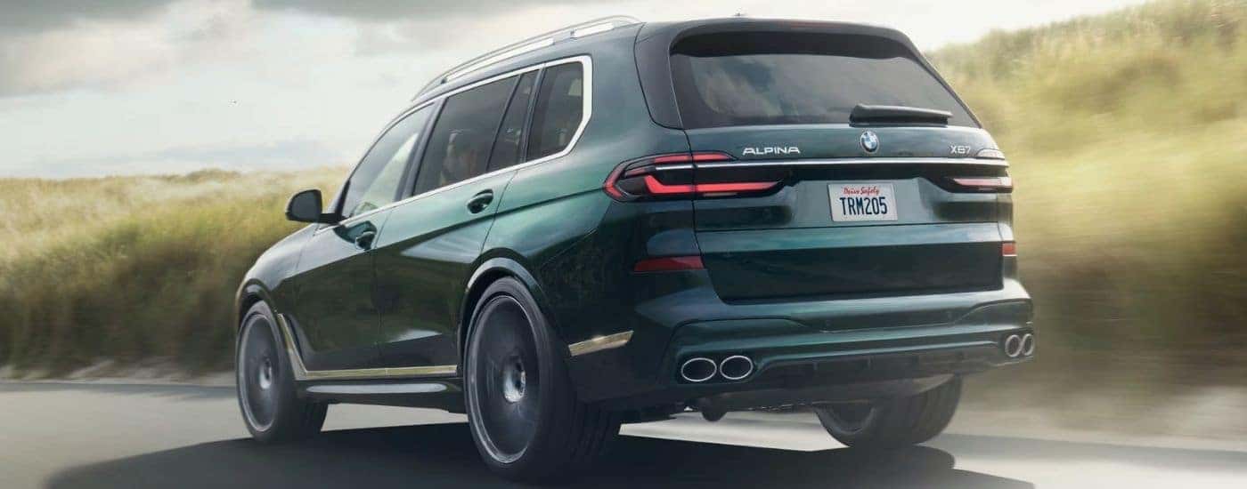 Rear view of a green 2025 BMW XB7 ALPINA driving on the road.