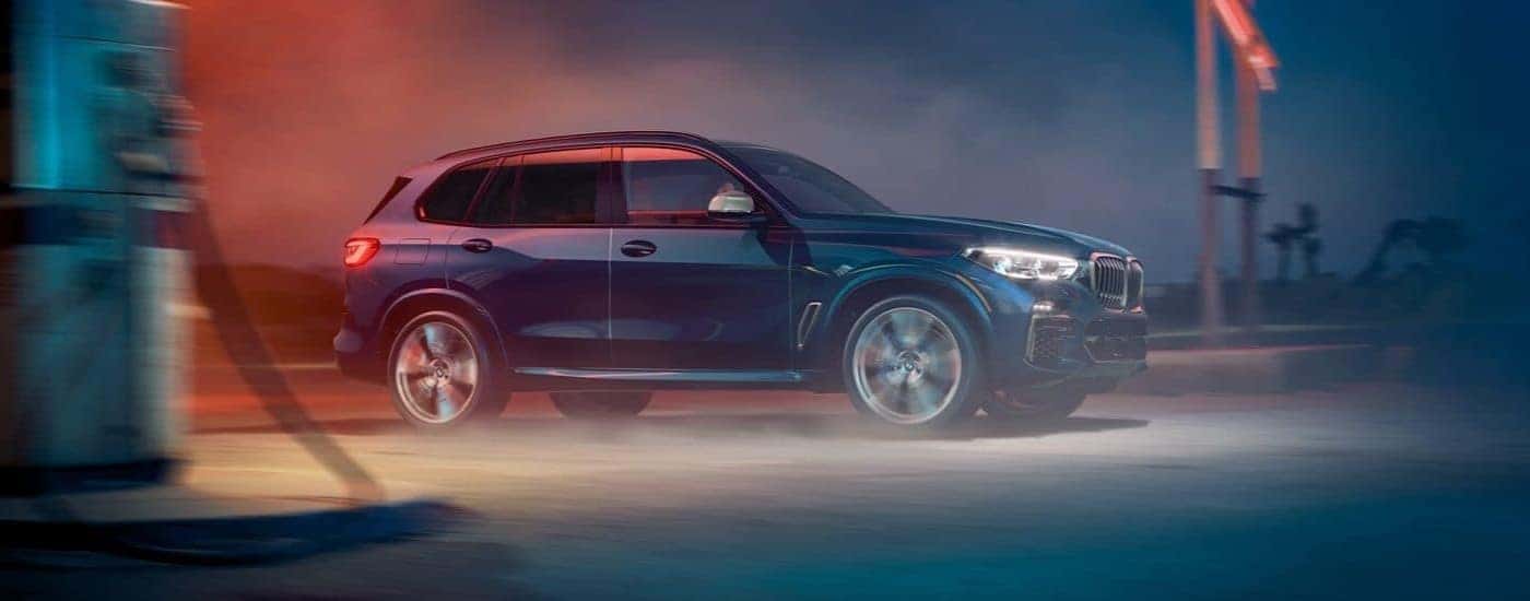 A blue 2020 BMW X5 SUV is shown driving near a gas station.