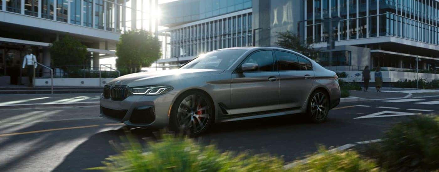A silver 2023 BMW 5 Series is shown driving on a city street.