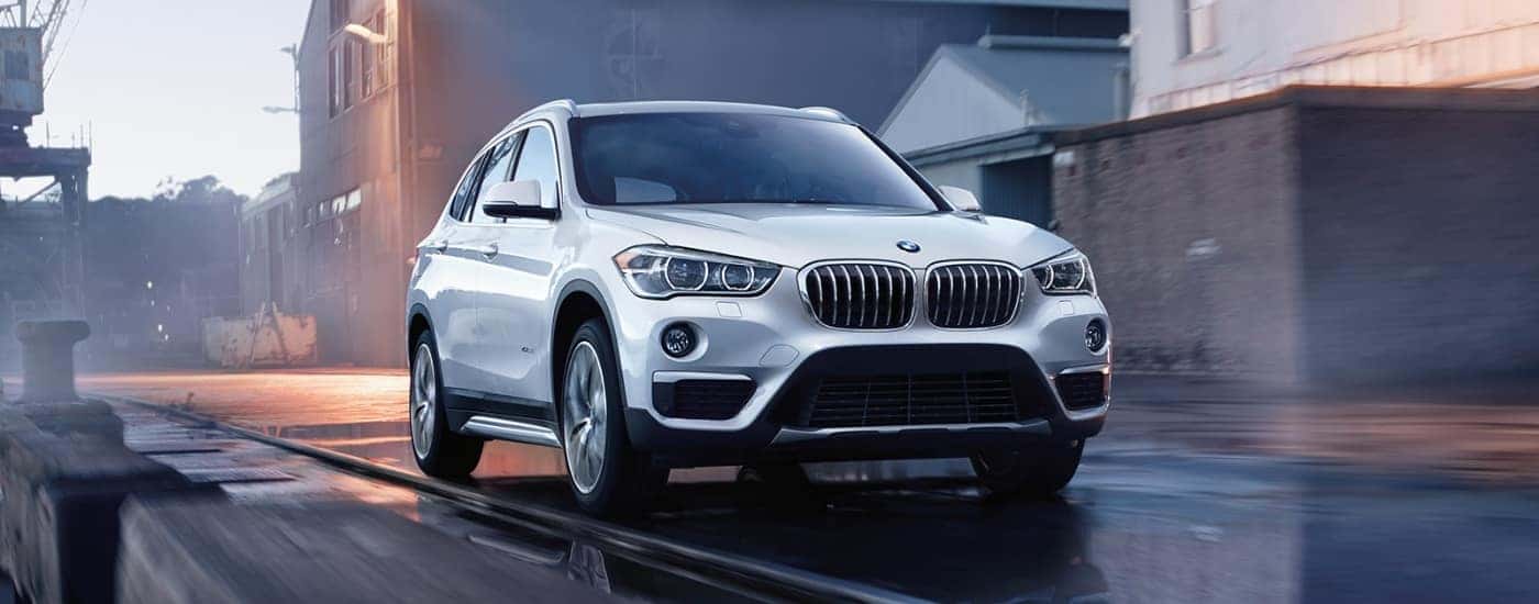 A white 2017 BMW X1 for sale is driving on wet pavement.