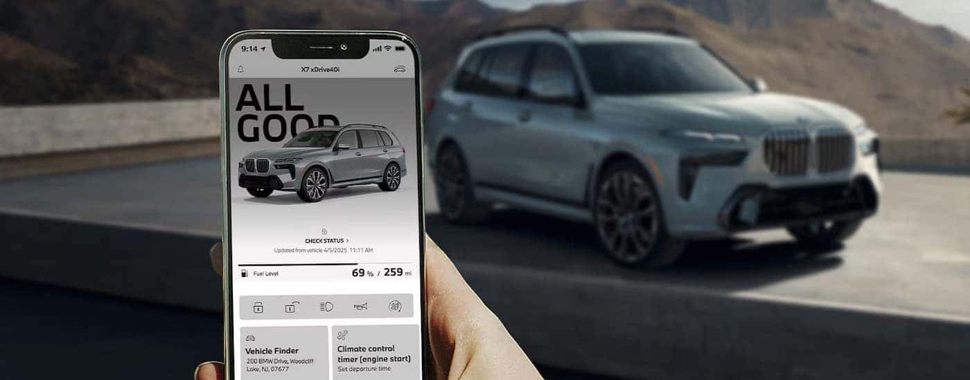 Person holding a cell phone near a blurred silver 202 BMW X7. 