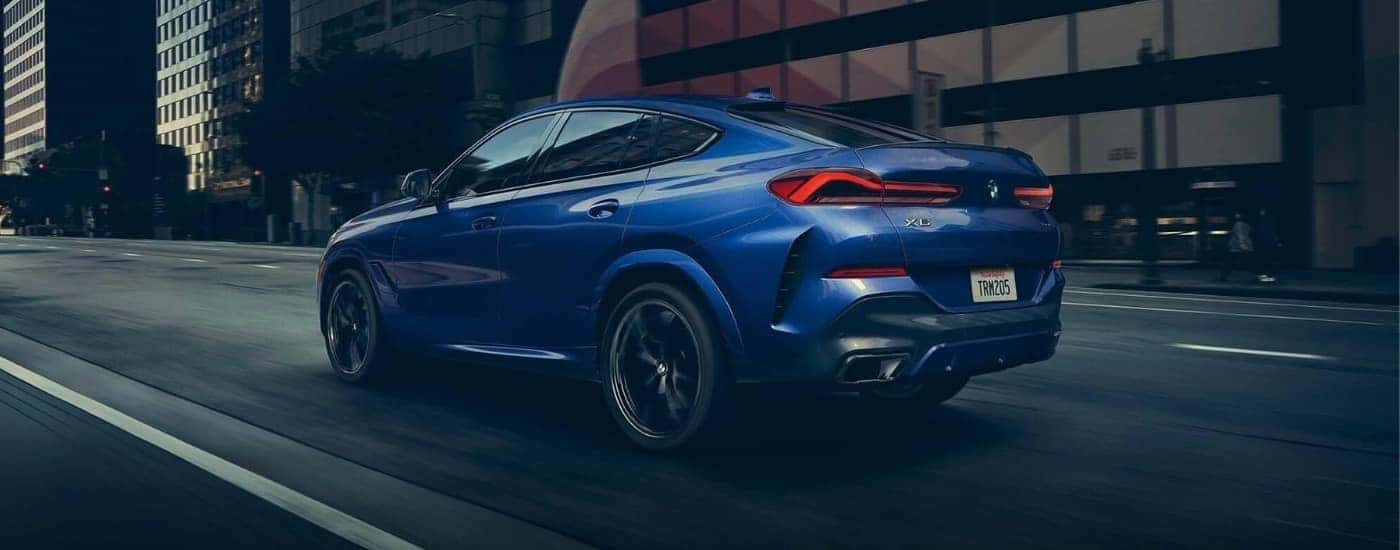 A blue 2022 BMW X6 is driving on a city street.