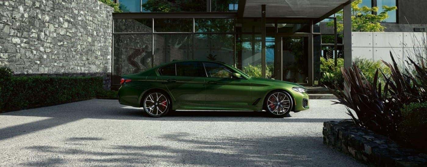 A green 2023 used BMW 5 Series for sale in Roanoke in front of a modern house.