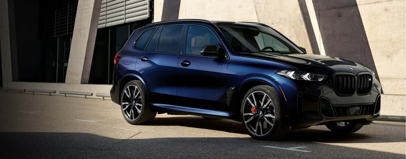 A blue 2024 BMW X5 M60i is shown parked near a modern building.