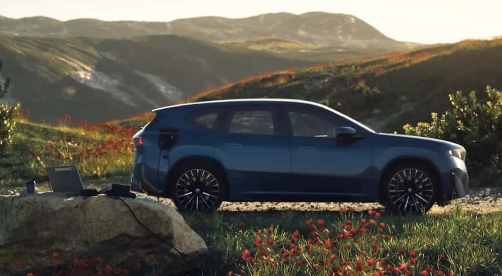A blue 2027 BMW iX3 parked near flowers.