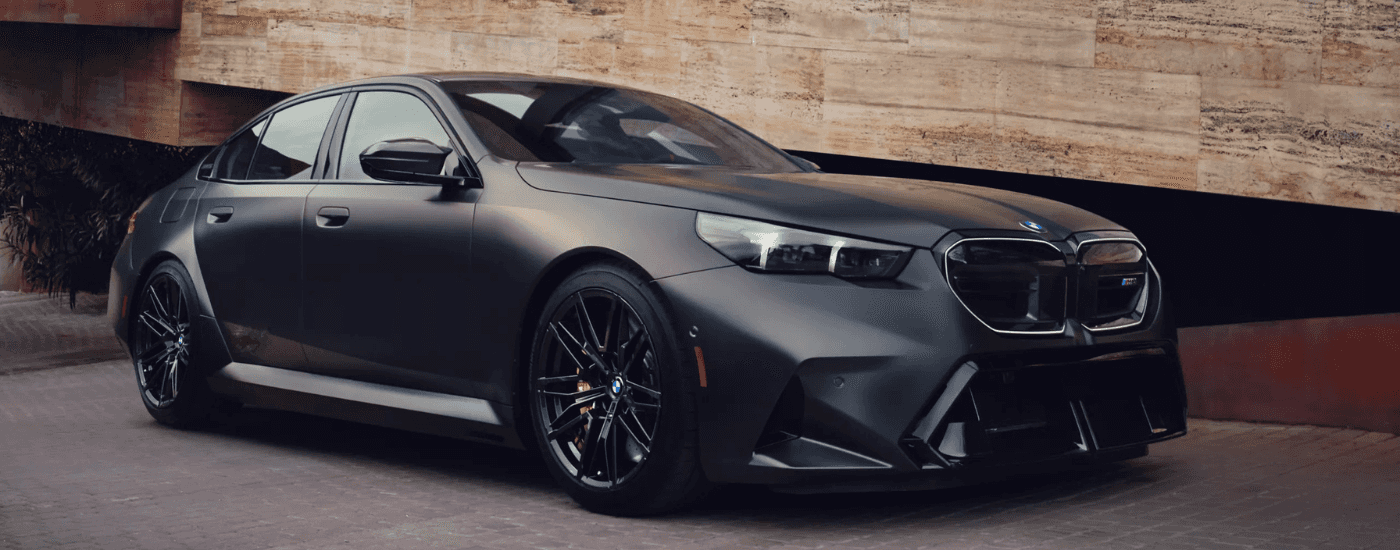 Black 2025 BMW M5 driving down the road from the side