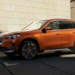 An orange 2025 BMW X1 parked in a city.