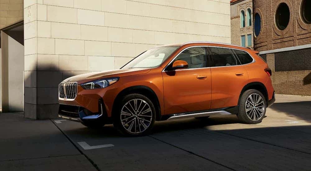An orange 2025 BMW X1 parked in a city.