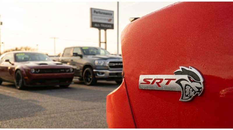 Close-up of the Dodge SRT badge with a used Dodge Challenger and RAM truck in the background.