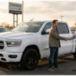 Customer and dealership representative shaking hands beside a used RAM truck in Woodbury, NJ after financing approval.